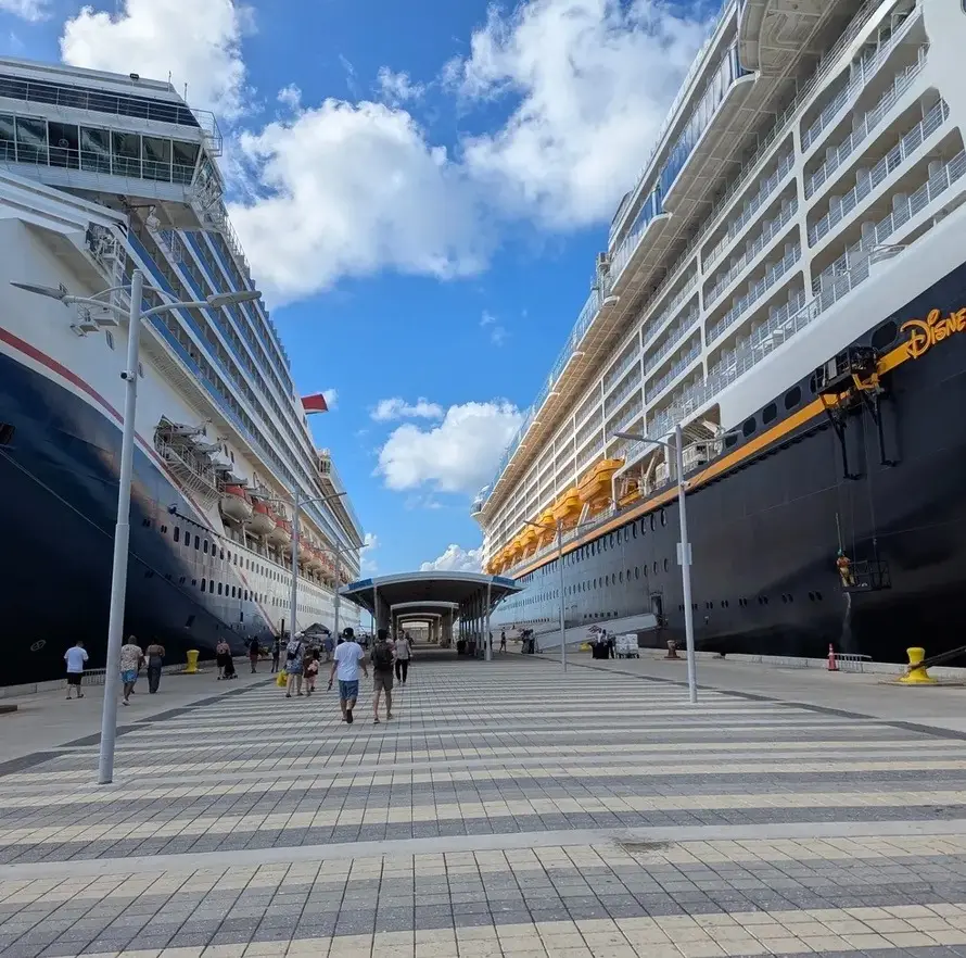 Disney cruise ship at Port Canaveral on embarkation day with the Disney Fantasy visible on the right with its yellow hull under a blue sky.