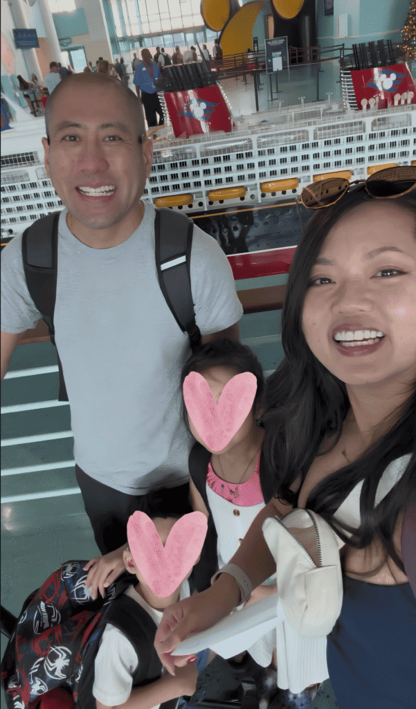 Family taking a picture in front of small disney cruise ship embarking on the disney fantasy ship.
